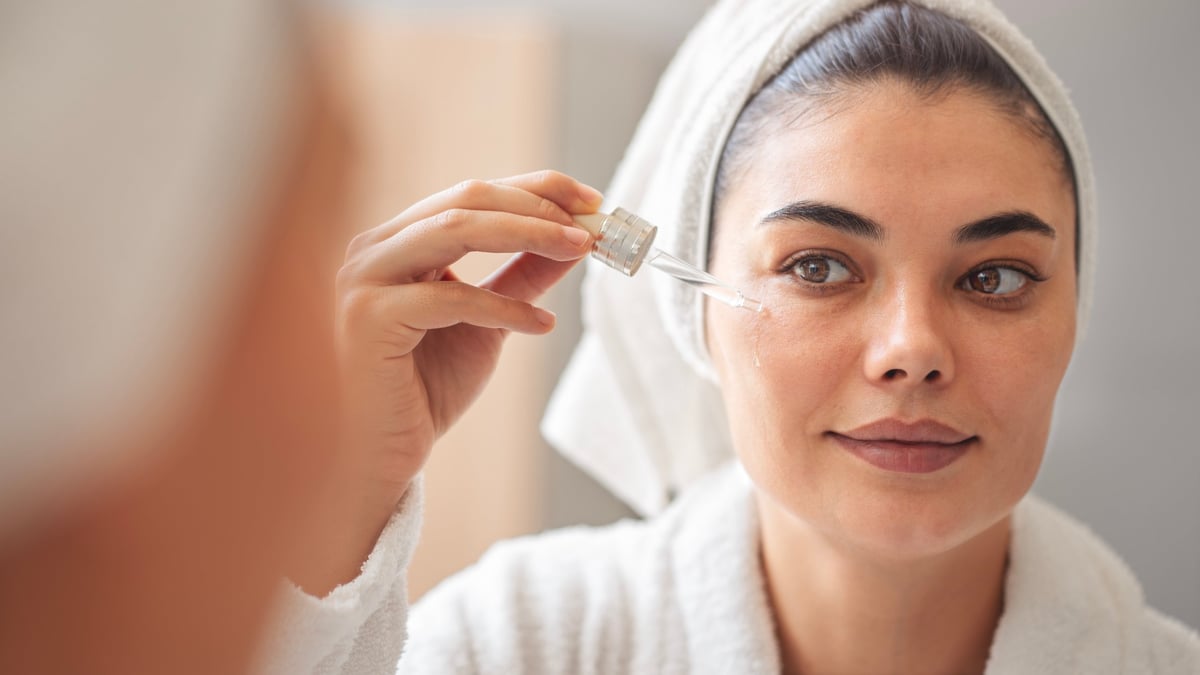 Beautiful woman applying serum in mirror